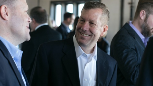 two men wearing suits having a conversation in a room with other people in the background