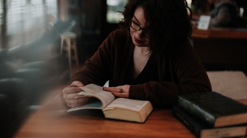 a woman sitting at a table reading a Bible