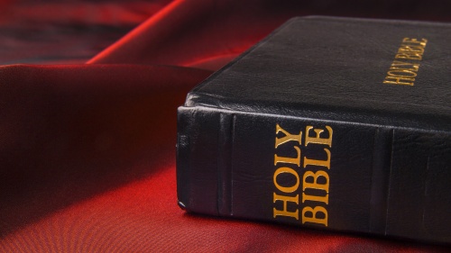 A Holy Bible laying on a table with a red table cloth.