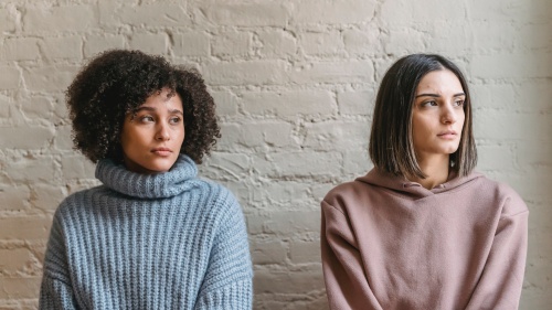 two woman standing against a wall and looking upset