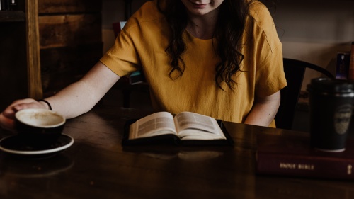 a woman sitting at a table with an open Bible and a coffee mug