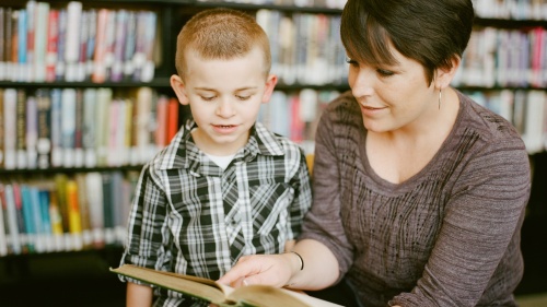 a woman and a child reading a book together with bookshelves in the background