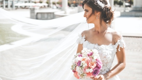 a bride holding a bouquet of flowers with her veil blowing in the breeze