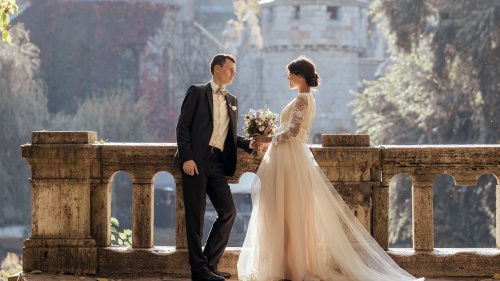 a groom and bride standing against a balcony with historic buildings in the background