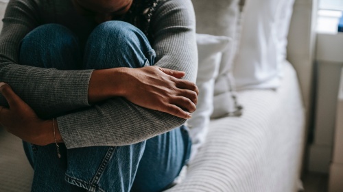 a woman sitting on a bed with her arms wrapped around her knees and her head down