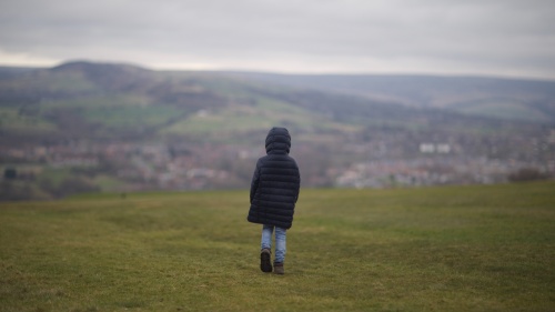 Child in black jacket walking on grass field during daytime.