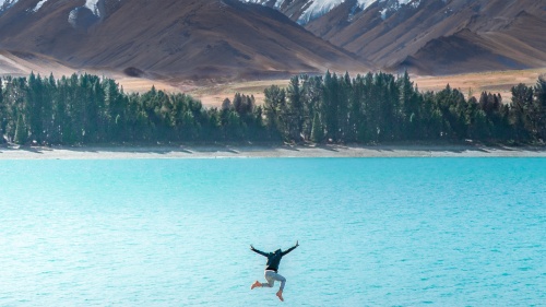 a person jumping in midair above a lake against a mountain backdrop