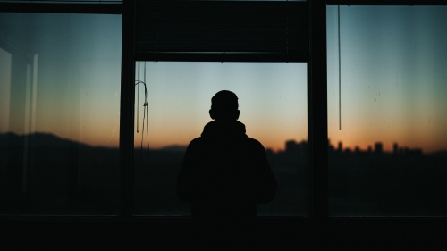 A silhouette of man standing by a window.