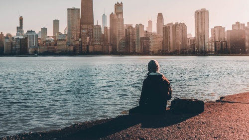 A person sitting near the edge of water looking at a city skyline.