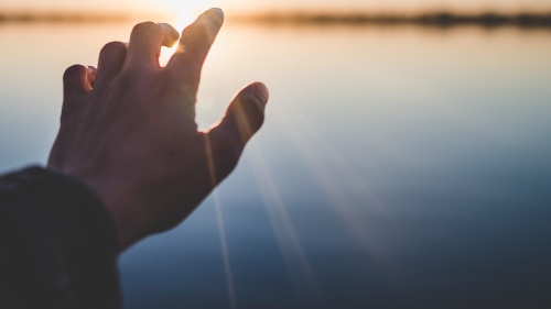 A hand reaching out over water. 