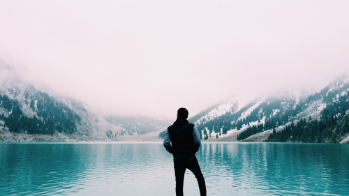 A man staring a clear blue lake.