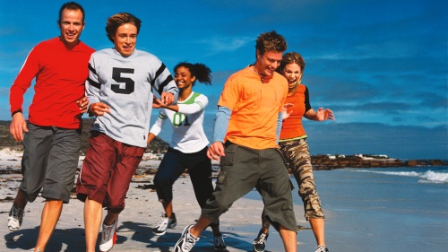 Young adults running on the beach.