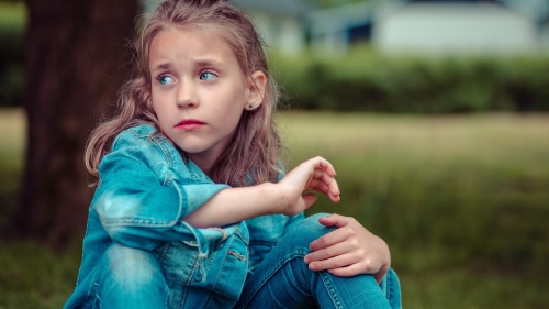 A little girl sitting on the grass looking sad.