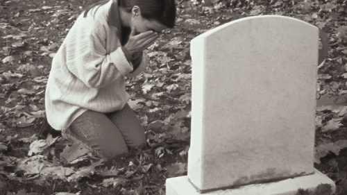 A woman crying by a grave stone.