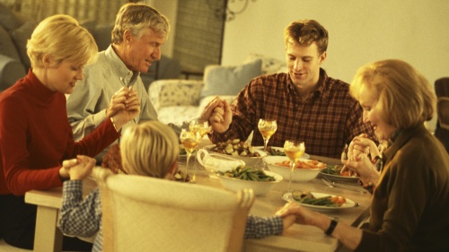 A family holding and praying before eating a meal.