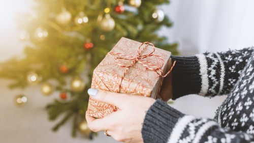 A person holding a wrapped gift in front of a Christmas tree.