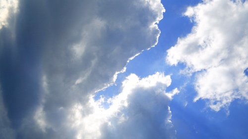 A blue sky with clouds and sun rays.