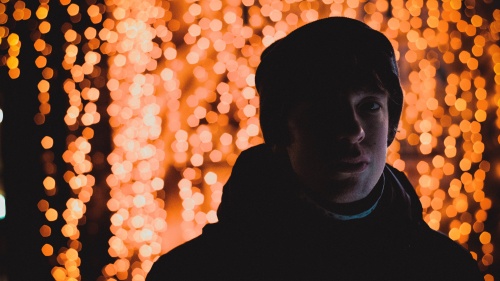 A young man standing in front of red lights.