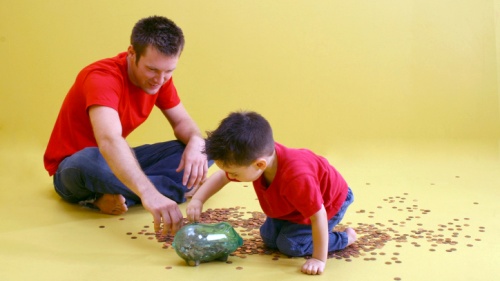 A father and son counting pennies from a glass jar.