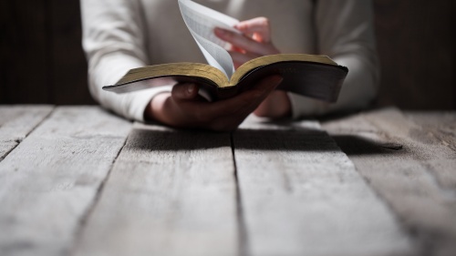 A person reading a Bible while sitting a table.