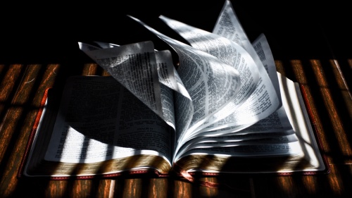 A Bible laying on table and the pages are blowing in a breeze.