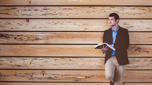 A man standing with a Bible with his back against a wall.