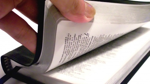 A person's hand thumbing through a Bible. 