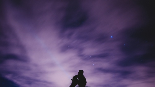 A person sitting on a hill with the stars in background.