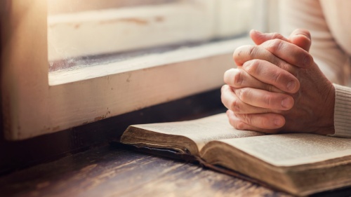 A woman reading a Bible by a window.