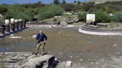 Scott Ashley standing at the edge of the harbor at Miletus, with the silted-in harbor and the remains of the monument behind him at the right. 
