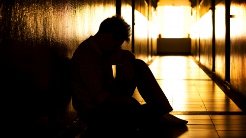 A person sitting with the head down in a dark hallway.