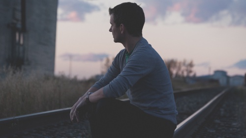 A young man sitting by an old railroad track.