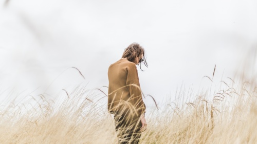 A woman standing in tall grass looking down.