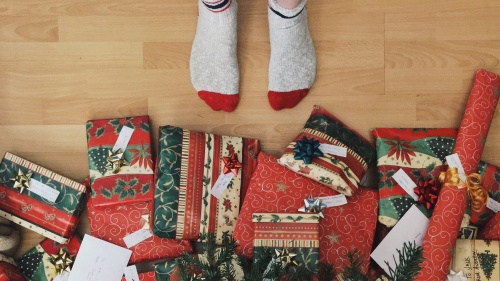 A person with socks standing right beside Christmas gifts. 