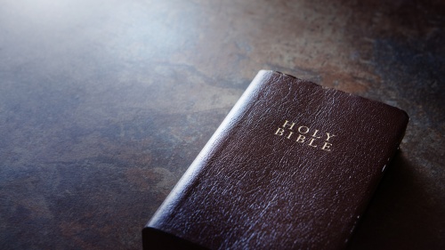 A Bible laying on a brown table.