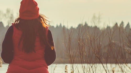 A woman wearing a jacket sitting outside looking at a lake.