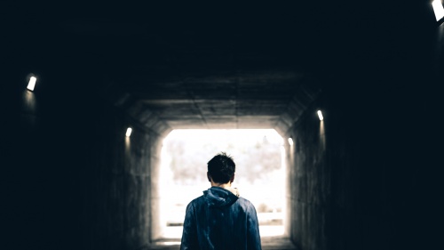 A man walking in a dark tunnel with light at the very end.