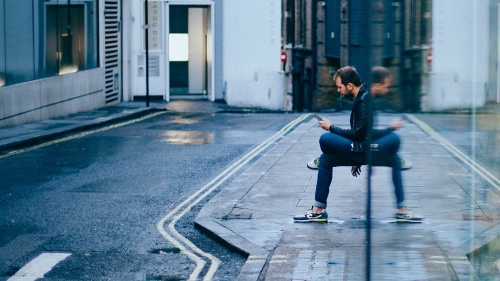 A man sitting by a building looking at his phone.