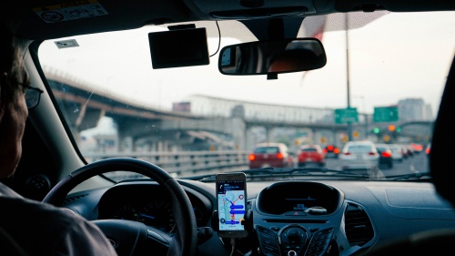 The perspective of sitting in the back seat of a car while a man is driving in city traffic.