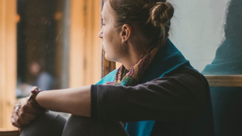 A woman sitting by a large window looking outside.