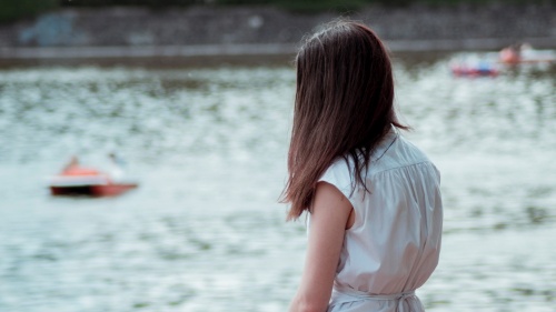 A teen girl sitting by a small pond looking out over the water.