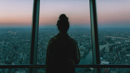 A woman looking outside of window of tall building.