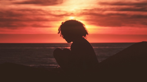A silhouette of young woman with the sun setting in the background.