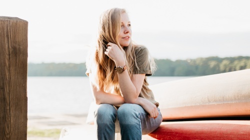 A young woman sitting on the edge of kayak that is on the shore.