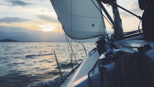 A sailboat gliding across the sea early in the morning.