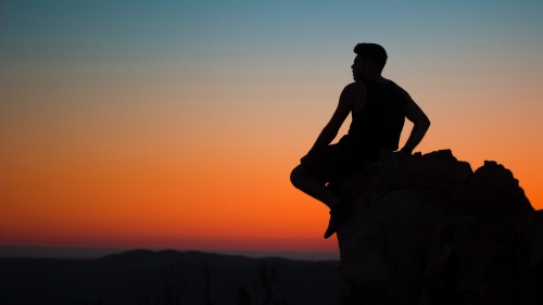 A man sitting on a rock with red sunset behind him.