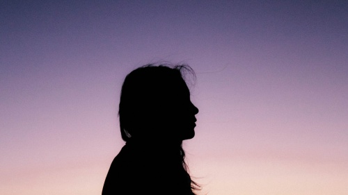 A silhouette of young woman with the sun setting in the background.