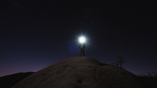 A person with a head lamp shining bright in the darkness.