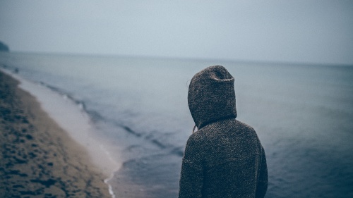 A person walking on a beach wearing a hoodie.