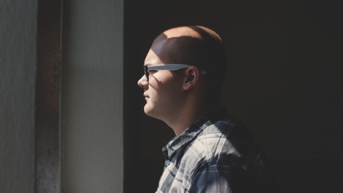 A man wearing glasses looking outside a window.